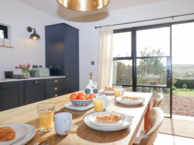 A kitchen with a wooden table set for breakfast with croissants juice and mugs at Church Farm Dairy in Cadbury near Thorverton