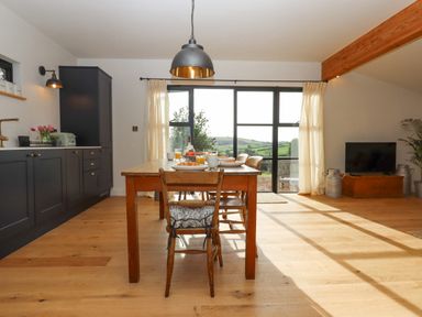 A kitchen dining area with a wooden table and chairs near large windows showing countryside at Church Farm Dairy Cadbury near Thorverton