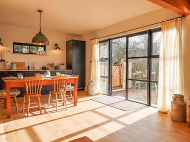 A kitchen dining area with wooden table and chairs next to large glass doors and curtains at Church Farm Dairy Cadbury near Thorverton