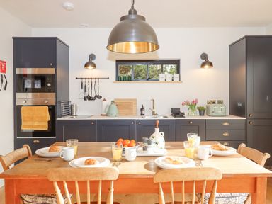 A kitchen with navy cabinets wooden table set with plates croissants glasses of juice and mugs at Church Farm Dairy Cadbury near Thorverton