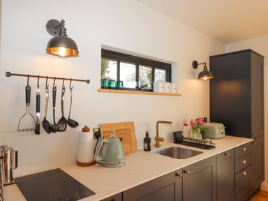A kitchen counter with utensils hanging a kettle a sink and flowers at Church Farm Dairy Cadbury near Thorverton