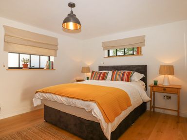 A bedroom with a bed orange blanket bedside tables lamps and windows at Church Farm Dairy Cadbury near Thorverton
