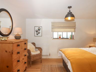 A bedroom with a wooden dresser mirror wicker chair and bed with a yellow blanket at Church Farm Dairy Cadbury near Thorverton