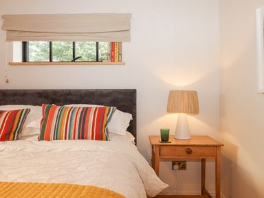 A bedroom with a bed with striped pillows a wooden nightstand with a lamp and a green glass at Church Farm Dairy Cadbury near Thorverton