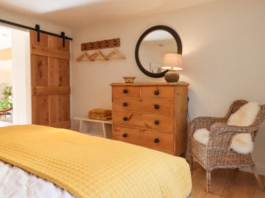 A bedroom with a yellow bedspread wooden dresser round mirror wicker chair and wooden sliding door at Church Farm Dairy Cadbury near Thorverton