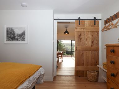 A bedroom with a wooden sliding door open to a dining area with a large window showing a countryside view at Church Farm Dairy Cadbury near Thorverton