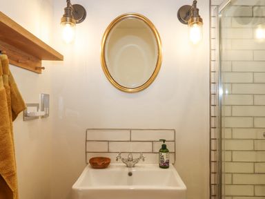 A bathroom sink with a round mirror and two wall lights above it and a shower area to the right at Church Farm Dairy Cadbury near Thorverton