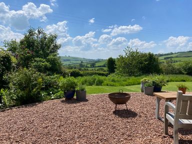 A garden with plants in pots a fire pit and outdoor furniture overlooking green hills at Church Farm Dairy Cadbury near Thorverton