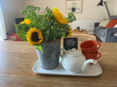 A tray with sunflowers in a pot, a teapot, red cups and a book in a living room at Church Farm Dairy Cadbury near Thorverton