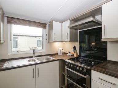 A kitchen with a double sink under a window a gas stove with an oven and a range hood white cabinets and wooden countertops at Swan in Shobdon