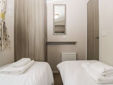 A small bedroom with two single beds each with folded white towels a wooden wardrobe a wall mirror and a door at Swan in Shobdon