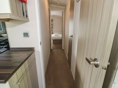 A narrow hallway with wooden doors on the right and a kitchen counter on the left leading to a bedroom with a bed at Swan in Shobdon
