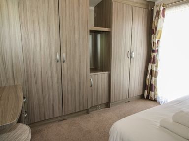 A bedroom with wooden wardrobes a bed with folded towels and patterned curtains at Swan in Shobdon