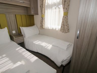 A bedroom with two single beds towels on the beds a wooden wardrobe and a window with patterned curtains at Swan in Shobdon