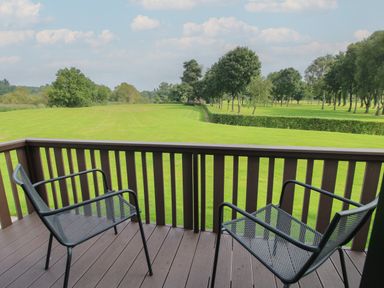 A balcony with two metal chairs overlooking a green lawn and trees at Swan in Shobdon