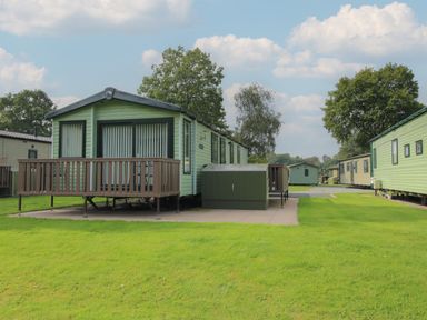 A green mobile home with a wooden deck on a grass lawn with other mobile homes nearby at Swan in Shobdon