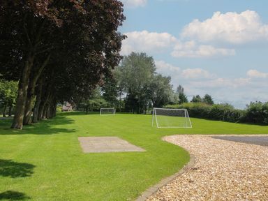 A grassy field with two soccer goals trees on the left and a gravel path on the right at Swan in Shobdon
