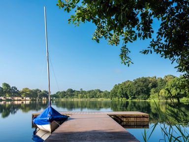 A dock with a sailboat and trees by a lake at Swan in Shobdon