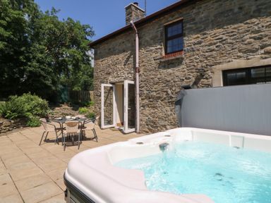 An outdoor patio with a hot tub and table with chairs at Felin Gogoyan Tregaron
