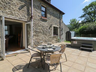 An outdoor patio with a table and chairs and a hot tub at Felin Gogoyan in Tregaron