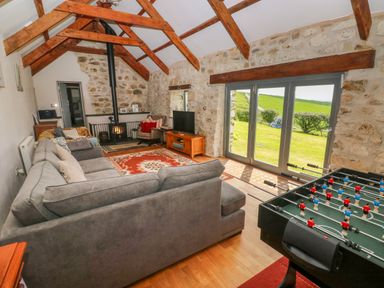 A living room with a grey sectional sofa a wood stove a foosball table and glass doors opening to a garden at Bryn Nante in Morvil near Maenclochog