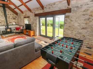 A living room with a foosball table near glass doors and a wood burning stove at Bryn Nante in Morvil near Maenclochog