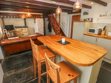 A kitchen with wooden countertop island and chairs next to a living area with a leather sofa and stove at Bryn Nante in Morvil near Maenclochog