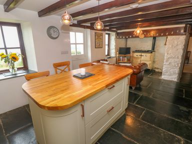 A kitchen with a wooden island and chairs near a living area with a sofa and stove at Bryn Nante Morvil near Maenclochog