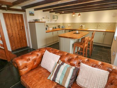 A kitchen with wooden countertops and island with two wooden stools and a leather sofa with cushions in the foreground at Bryn Nante in Morvil near Maenclochog