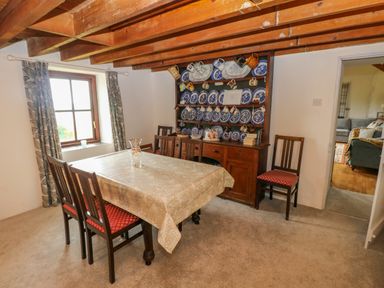 A dining room with wooden chairs a table covered with a tablecloth and a cabinet displaying blue and white plates and mugs at Bryn Nante in Morvil near Maenclochog