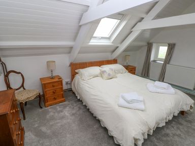 A bedroom with a double bed two bedside tables with lamps a wooden chair a window and a skylight at Bryn Nante in Morvil near Maenclochog