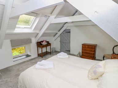 A bedroom with a skylight and small window a wooden side table with a pink pitcher a wooden chest of drawers and a bed with white linens at Bryn Nante in Morvil near Maenclochog