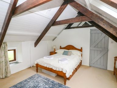 A bedroom with a wooden bed frame a bedside table with a lamp a blue rug a window with curtains and exposed wooden beams on the ceiling at Bryn Nante in Morvil near Maenclochog