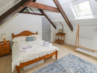 A bedroom with a double bed bedside tables a window skylight wooden beams and a blue patterned rug at Bryn Nante in Morvil near Maenclochog
