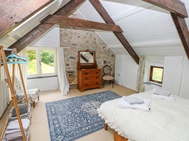 A bedroom with wooden beams and a stone wall with chest of drawers mirror chair and bed at Bryn Nante in Morvil near Maenclochog