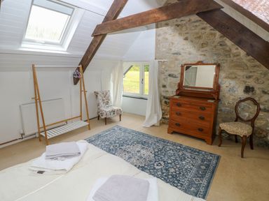 A bedroom with a bed towels a wooden dresser with mirror two chairs a window and wooden beams at Bryn Nante Morvil near Maenclochog