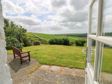 A garden with a wooden bench on gravel and green fields beyond viewed from a doorway at Bryn Nante in Morvil near Maenclochog