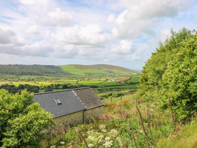 A stone building with a slate roof surrounded by greenery and fields with hills in the distance at Bryn Nante in Morvil near Maenclochog
