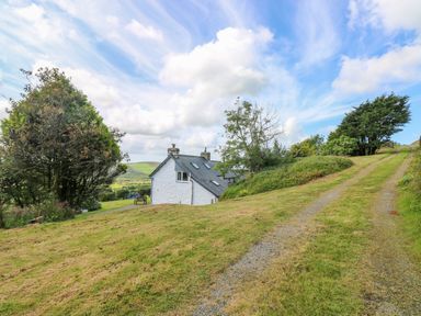 A white house with a slate roof surrounded by trees and grassy hills with a gravel path at Bryn Nante Morvil near Maenclochog