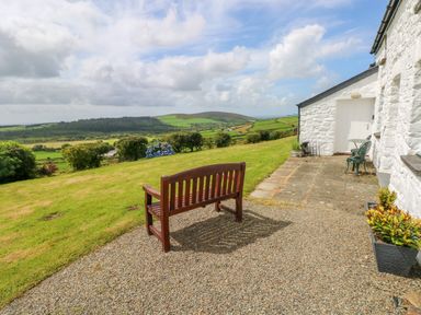 A garden area with a wooden bench, metal chairs, and a stone patio at Bryn Nante in Morvil near Maenclochog