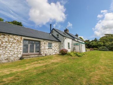A stone house with a grey roof and green lawn under a partly cloudy sky at Bryn Nante in Morvil near Maenclochog