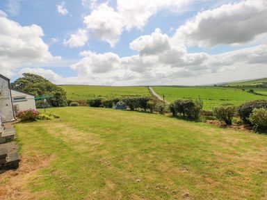 A grassy yard with bushes and a path leading into green fields at Bryn Nante Morvil near Maenclochog