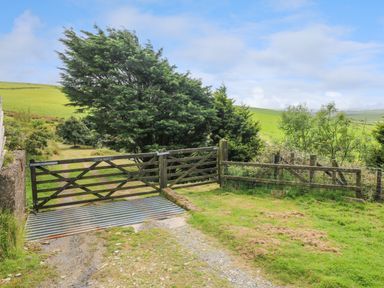 A wooden gate across a rural dirt path with cattle grid and trees in a countryside setting at Bryn Nante in Morvil near Maenclochog