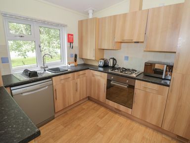 A kitchen with wooden cabinets black countertops a gas stove oven dishwasher microwave kettle and a window showing trees at Daffodil in Eardisland
