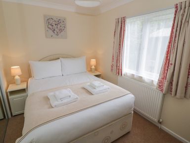 A bedroom with a double bed bedside tables with lamps a window with patterned curtains and a radiator at Daffodil in Eardisland