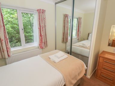A bedroom with a single bed white linens folded towels a window with patterned curtains mirrored closet doors and a wooden chest of drawers at Daffodil in Eardisland