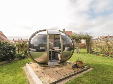 A garden with a round glass pod containing seating and a table at Coast Cottage in Bamburgh