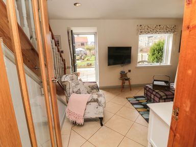 A living room with armchair near stairs wall mounted tv and window at Coast Cottage in Bamburgh