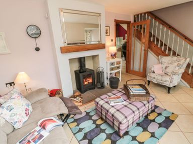 A living room with a fireplace sofa armchair ottoman rug and staircase at Coast Cottage in Bamburgh