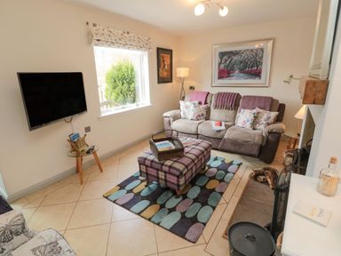A living room with a sofa a patterned rug and a wall-mounted TV at Coast Cottage in Bamburgh
